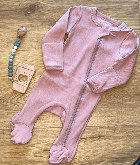 Pink baby onesie with a pacifier clip and teething ring on a wooden surface